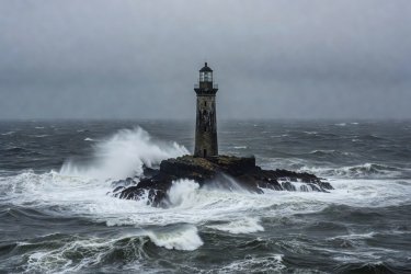 A lonely wave-lashed lighthouse tower against a storm grey ocean