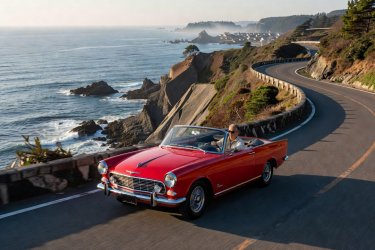 A red vintage automobile driving along a scenic coastal road in Japan